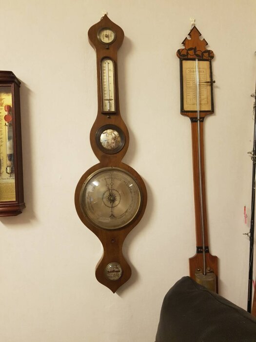Väggmonterad barometer och termometer i trä, med visartavla och glasfronter, visar vädermätningar.