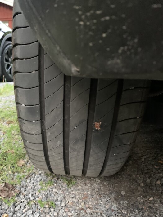 Bild på ett bildäck med en lagad pyspunka, taget ovanifrån. Däckets slitage och reparation syns tydligt på grusunderlag.