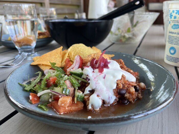 Chili con carne med nachos, ostsås, picklad rödlök, crème fraiche och sallad på grå tallrik.