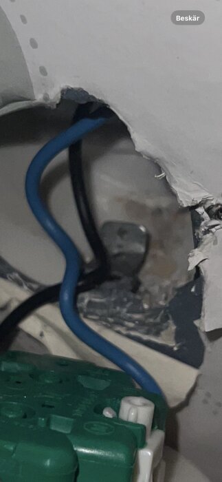 Elkabling och grön kopplingsdosa bakom en vägg med synlig metallring och blå kabel.