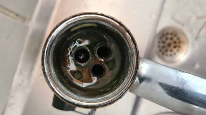 Närbild av insidan av ett metalliskt rör med tre hål, delvis täckt av grönaktig beläggning. Kontext: fråga om hur man når en gummipackning.