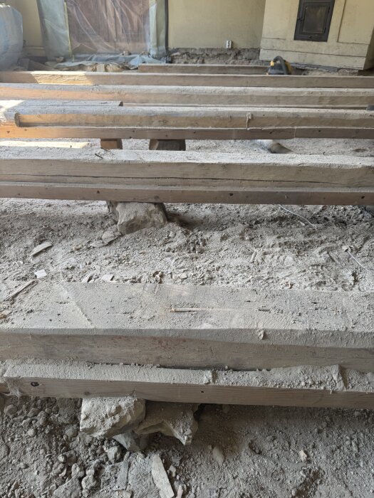 Renovering av krypgrund med bjälkar som ligger på stenar, visar borttagen isolering och jordgolv med dammiga ytor.