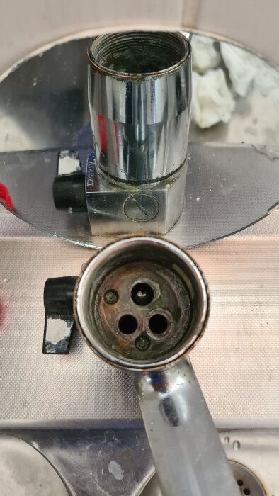 Kran med delvis borttaget vridreglage, med synliga skruvhål och spegelåterspegling i bakgrunden.