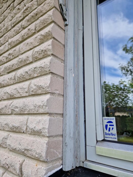 Närbild av träfoder vid ett fönster, där färgen har börjat flagna. Fodret är monterat mot en fasad av ljus tegel.
