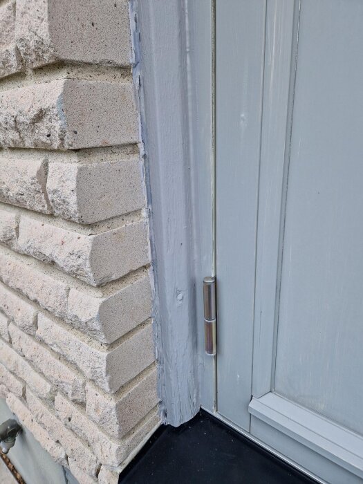 Slitet fönsterfoder i trä bredvid tegelvägg med gångjärn synligt.