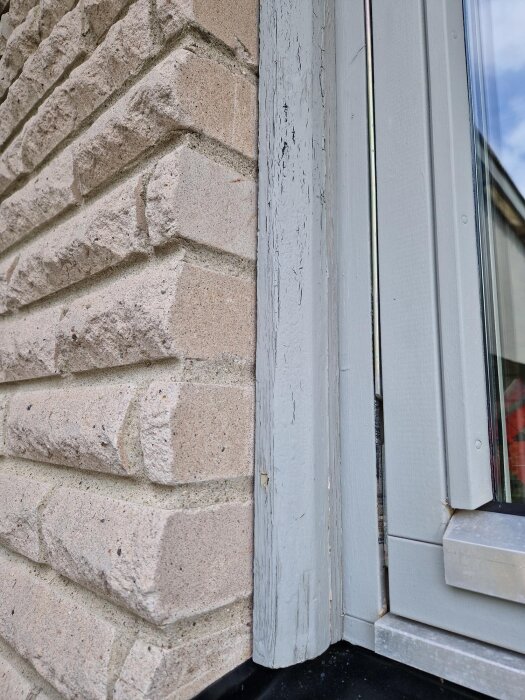 Fönsterfoder i trä med flagnande färg bredvid tegelvägg.