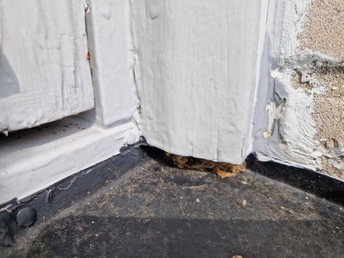 Slitet vitt fönsterfoder och murverk med synliga sprickor och avflagad färg, med smutsig tröskel i förgrunden.