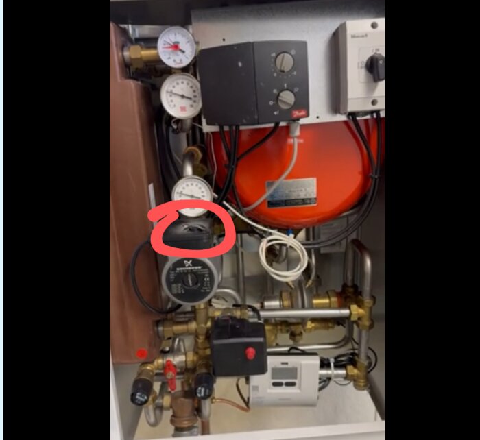 Cirkulationspump med röd markering i ett tekniskt system med rör, tryckmätare och ledningar.