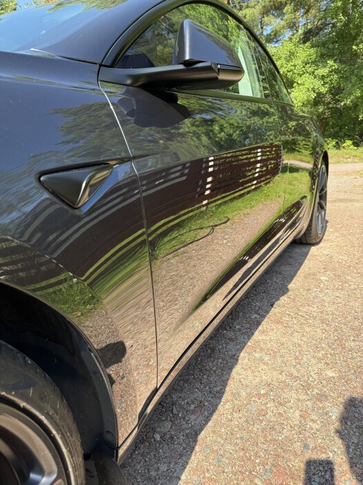 Svart Model 3 2024 med polerad yta reflekterar omgivningen, fotograferad utomhus på en solig dag. Lacken ser blank och ren ut.