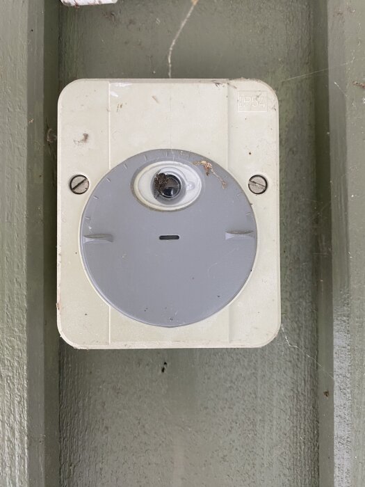 Skymningsrelä monterat på vägg med IP54-märkning, synliga skruvar och viss smuts och spindelväv runt om.