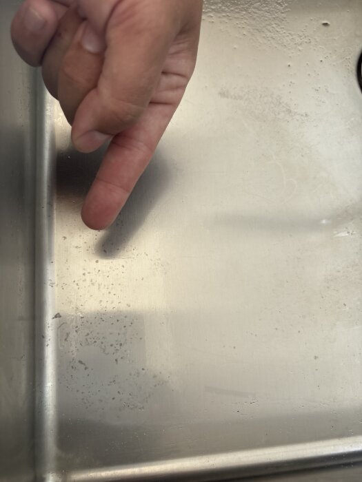 Hand pekar på fläckar i en rostfri diskho.