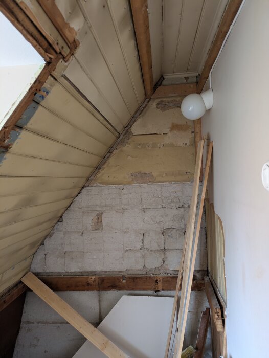 Gammalt kök under renovering med pärlspontfris, murad yttervägg och borttagna masonitskivor. Vägglampa och träreglar syns.