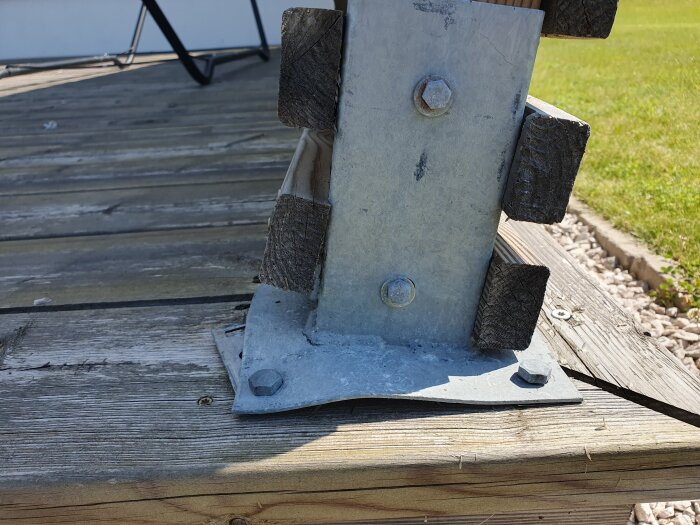 Metallplatta och stolpe på trätrall, del av insynsskyddskonstruktion med muttrar och bultar. Gräs och stenar syns i bakgrunden.