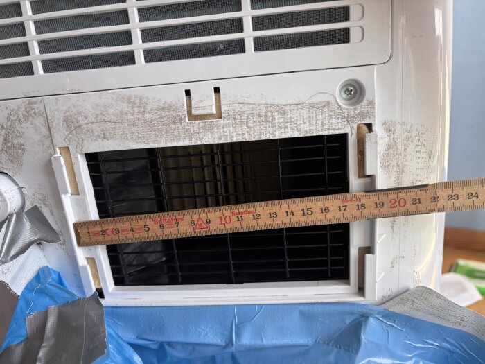 Öppning på en portabel AC med måttstock och tejp, där övergången för att koppla på luftslang saknas.