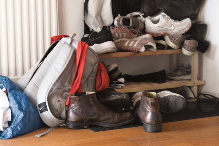 En DIY-skohylla med många skor, en ryggsäck och kläder. Hyllan är byggd i trä och placerad bredvid ett element. Skor står ovanpå och under hyllan.