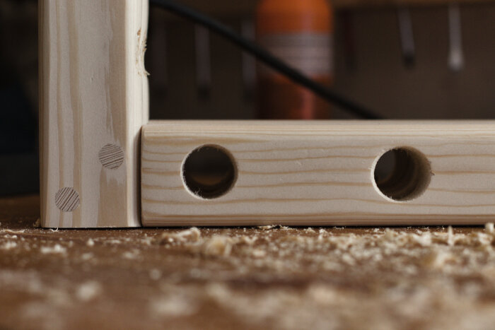 Trähylla med borrade hål och synliga pluggar i en konsol, del av skohylla av furu under konstruktion i verkstad.