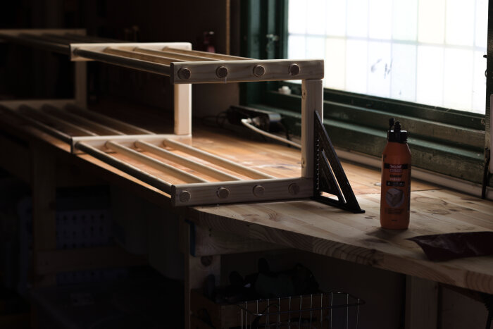 Hemmagjord skohylla i trä under konstruktion, placerad på en arbetsbänk bredvid lim och en vinkelhake.