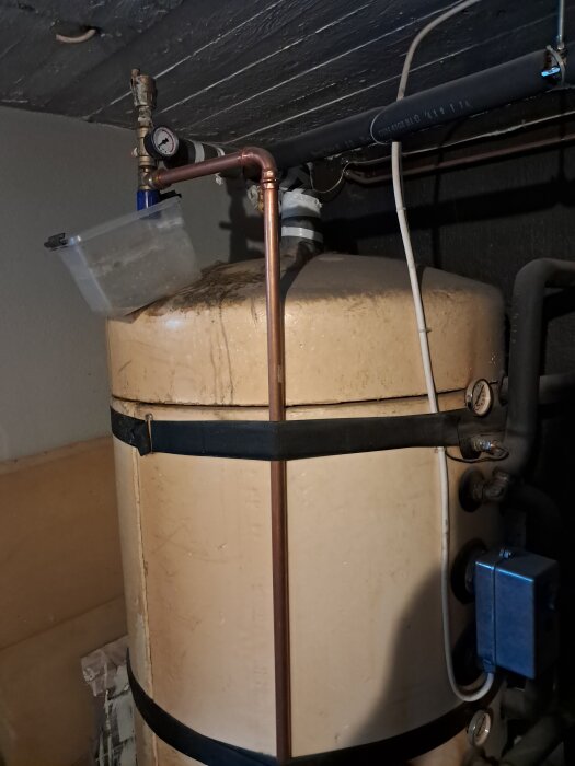 Ackumulatortank med ventiler och kopparrör, där ett kärl fångar upp vatten från en läckande ventil på toppen, noterat vid strömavbrott.