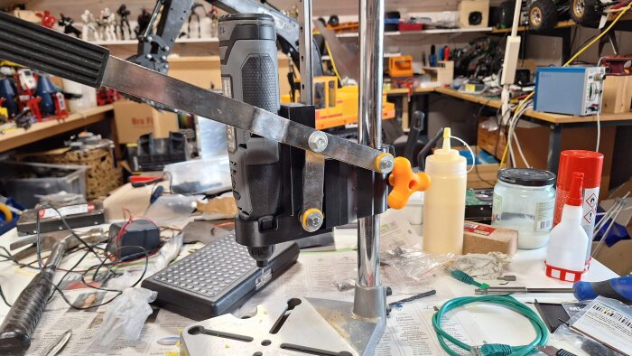 Borrstativ anpassat för ett multiverktyg på en arbetsbänk, omringat av verktyg och material. En fjäder saknas för full funktionalitet.