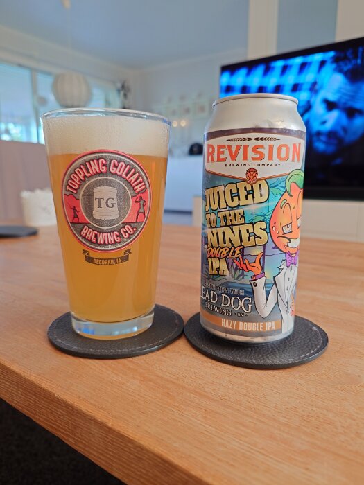 Ett glas öl bredvid en burk Revision Juiced To The Nines Double IPA på ett bord, med bakgrund av en påslagen TV.
