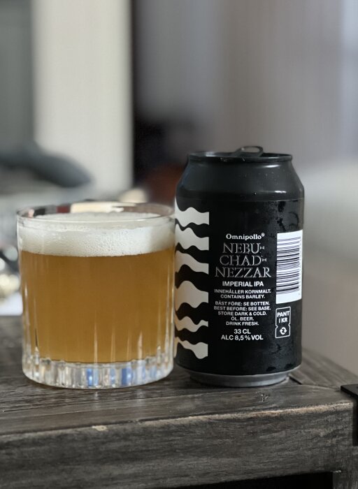 Svart burk Omnipollo Nebuchadnezzar Imperial IPA och ett glas fyllt med skummande öl på ett bord.