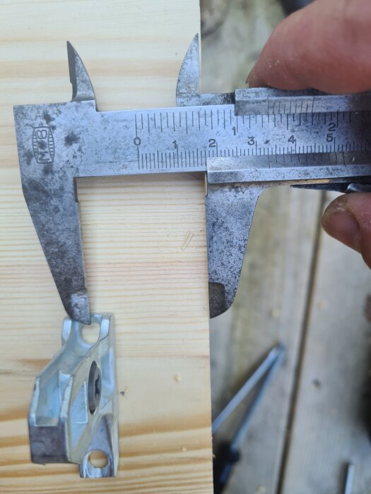 Mätning av avstånd från kant på träbit med skjutmått, del av lådfront för kök syns.