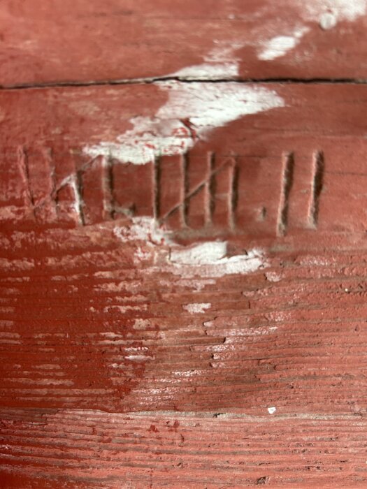 Inristade märken på en röd trävägg med avflagning, i ett gammalt timmerhus.