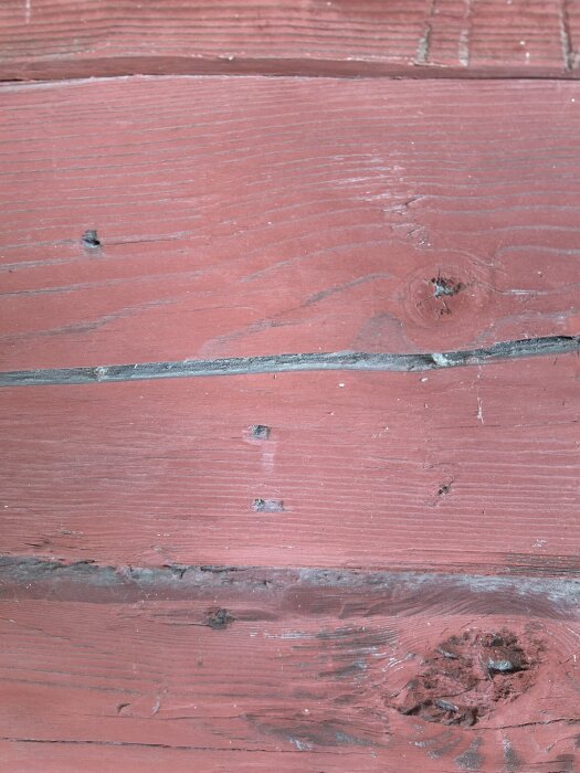 Rödmålade träplankor med spikhål och inskriptioner på ytan.