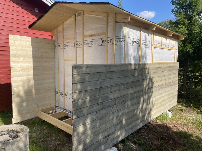 Byggprojekt pågår; träpanel har monterats på en konstruktion med synliga reglar och vindskydd, takutbyggnad syns ovanpå.