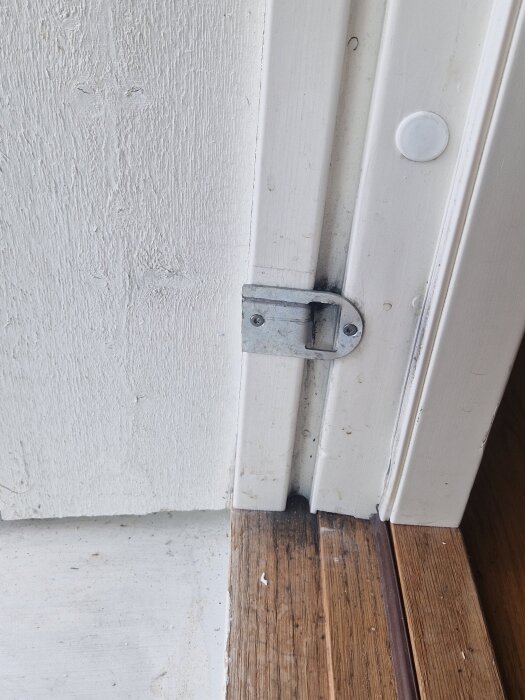 Närbild av en vit altandörr med ett metallbeslag, en spricka synlig ovan och till höger om dörrhandtaget, dörren är svår att låsa korrekt.