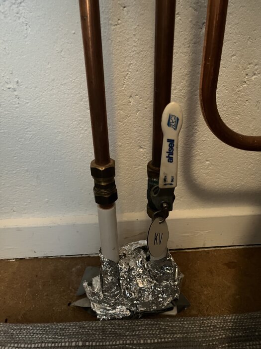 Ventiler och kopparrör med folie, märkt "KV", installerade på vit vägg och golv.