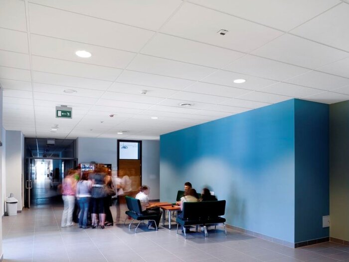 Interiör av ett rum med Ecophon-takplattor, folk som står och sitter vid bord, ljusblå vägg och moderna möbler.