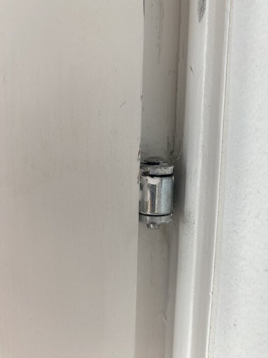 Gångjärn i en vit dörrkarm med fokus på dess metallstift; balkongdörrens justeringsproblem diskuteras.