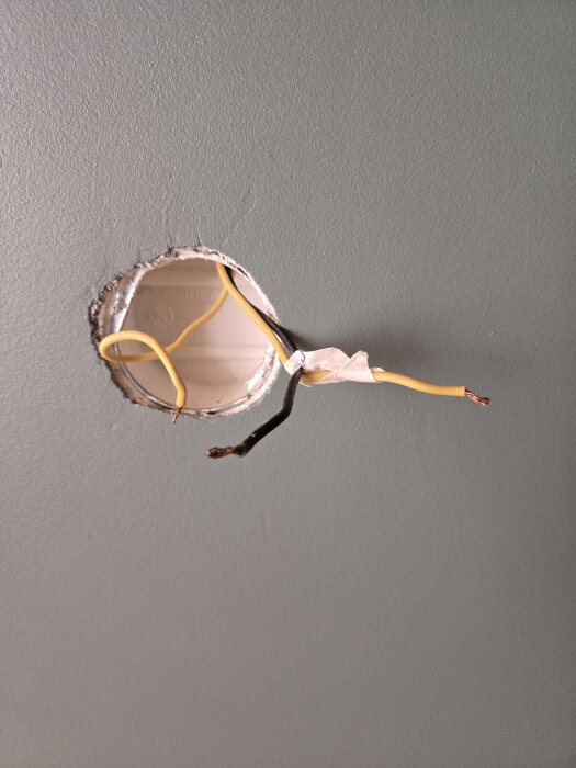 Vägg med uttagshål där svarta och gula elkablar syns; elkabelinstallation pågår.