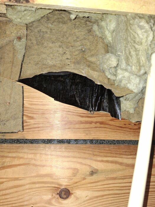 Isoleringsmaterial och svart papper på insidan av råspont i takkonstruktion, med trädstruktur synlig.