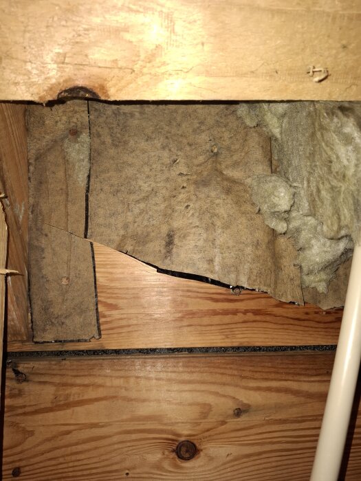 Brun papp på insidan av råspont i ett tak, möjlig asfaltpapp. Råsponten syns tydligt, omgärdad av isolering och träelement.