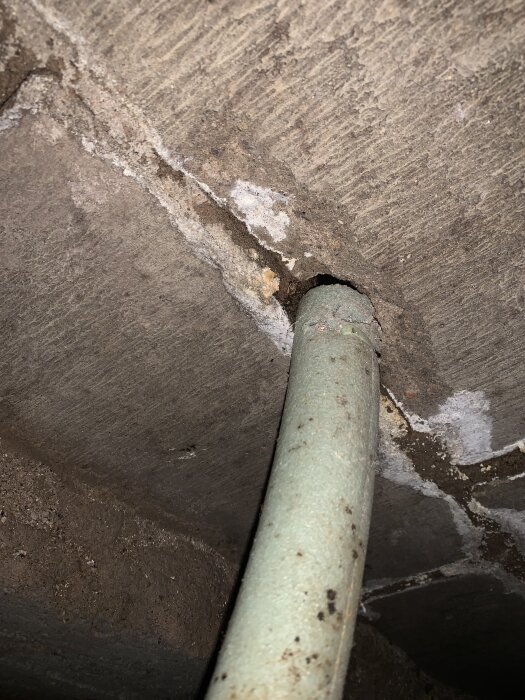 Slang genom hål i betong med fuktmärken och mörka kanter runt inmatningspunkten.