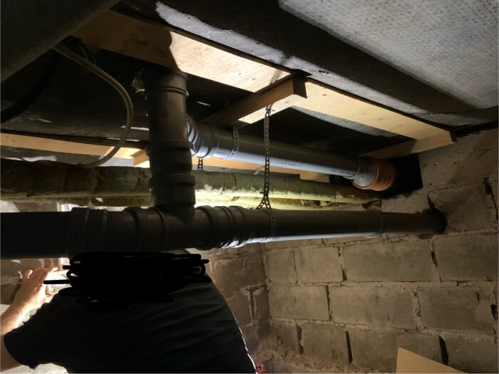 Avloppsrör i krypgrund med vattenläckor, visar också kondens på rören och isolering. Person i förgrunden som undersöker området.