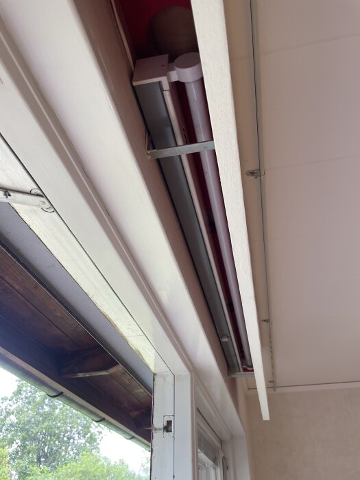 Träram med lysrör inuti, monterad ovanför ett fönster i ett vardagsrum från 1960-tals hus.