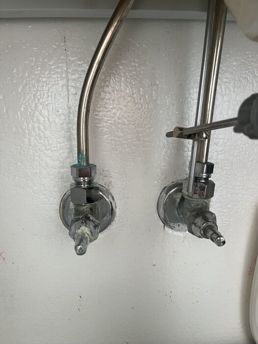 Kopplingar och rör under ett handfat med tecken på ärgning.