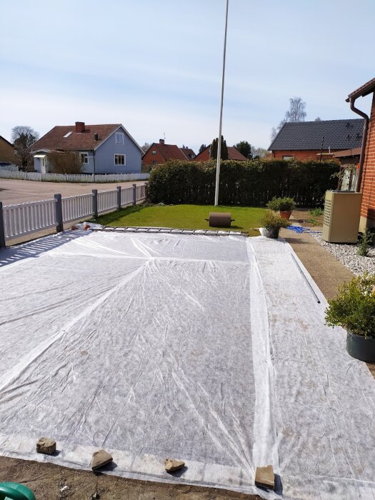 Trädgård täckt av fiberduk med stenar vid kanterna för att skydda mot avdunstning, stabilisera temperatur och hindra fåglar från att nå frön.