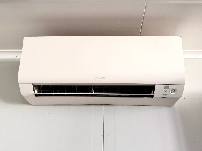 Vit Daikin luftkonditioneringsenhet monterad på en inomhusvägg, används för uppvärmning av ett garage.