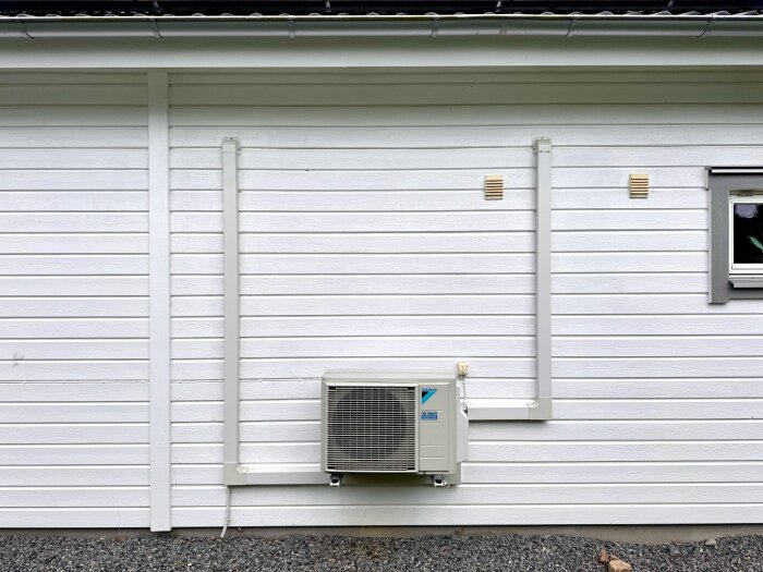 Utsidan av ett garage med en utomhusenhet av märket Daikin monterad på väggen.