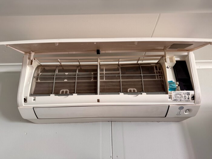 Inomhusdel av luftkonditionering med öppet filterlucka, med synliga filter och etikett.