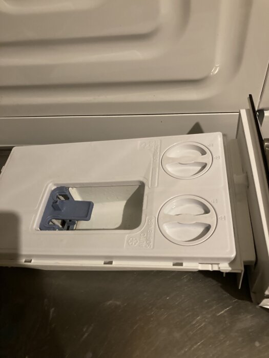 Tvättmedelsfack i Samsung tvättmaskin med två runda, gröna öppningar, högra med metallspiral, vänstra utan.