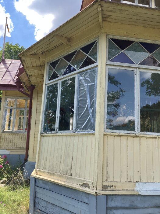 Glasveranda på äldre hus med sliten träpanel och trasigt fönster, del av ett renoveringsprojekt i sommarhus på ö i Mälaren.