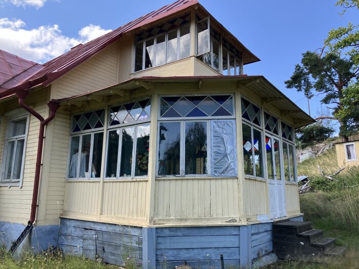 Gammal glasveranda i behov av renovering på ett sommarhus från 1890 i Mälaren, med färgflagor och trasiga fönster med färgat glas.