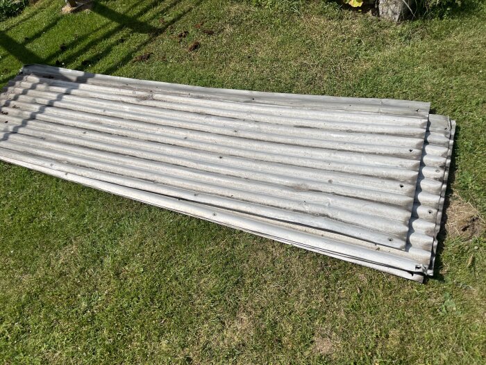 Rostiga korrugerade takplåtar med hål ligger på en gräsmatta, redo för återanvändning eller kassering efter ett misslyckat projekt.