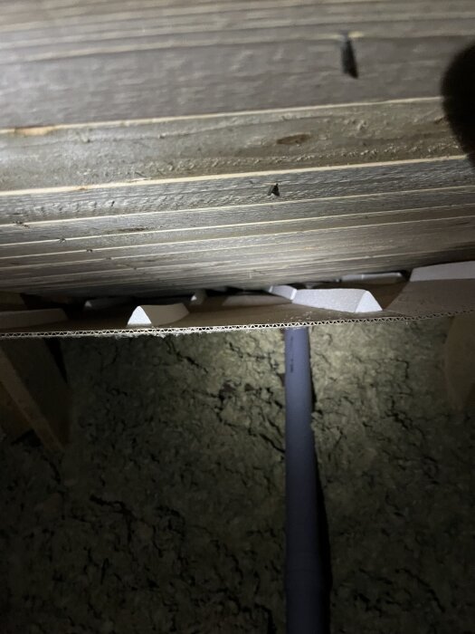 Bild av vinden med isolering och ett rör synligt under en träkonstruktion, tagen efter regn för att kontrollera fuktighet.