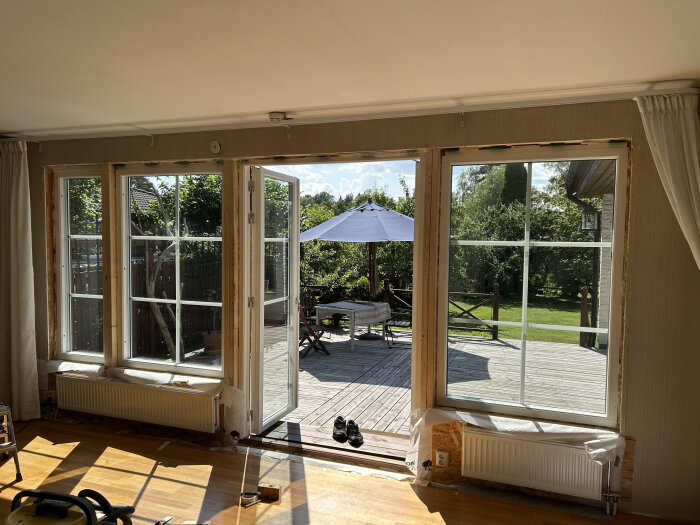 Bilden visar ett nyinstallerat fönsterparti i en 70-talsvilla, med utsikt över en trädäckad altan och trädgård, utan ångspärr synlig på insidan.